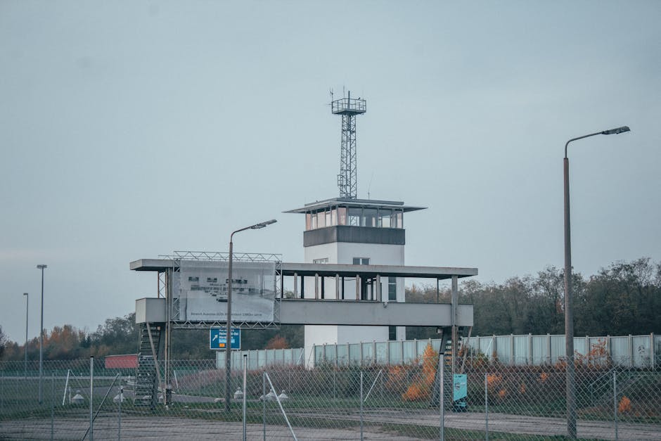 A modern control tower at an airport, surrounded by fences and street lamps.